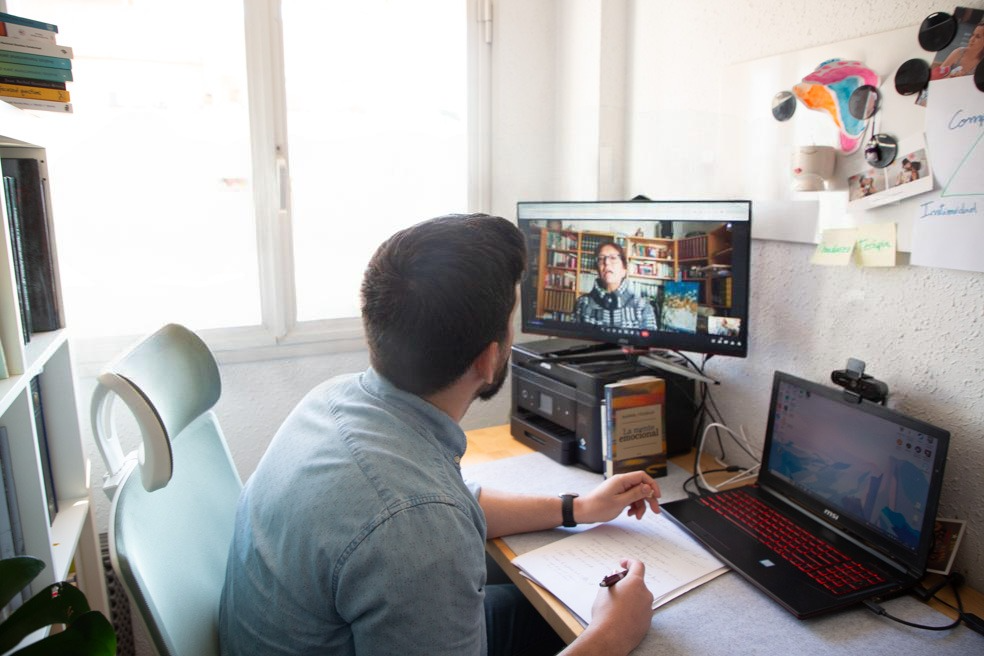 un psicóleg davant la pantalla de l'ordinador fent una sessió online i prenent apunts