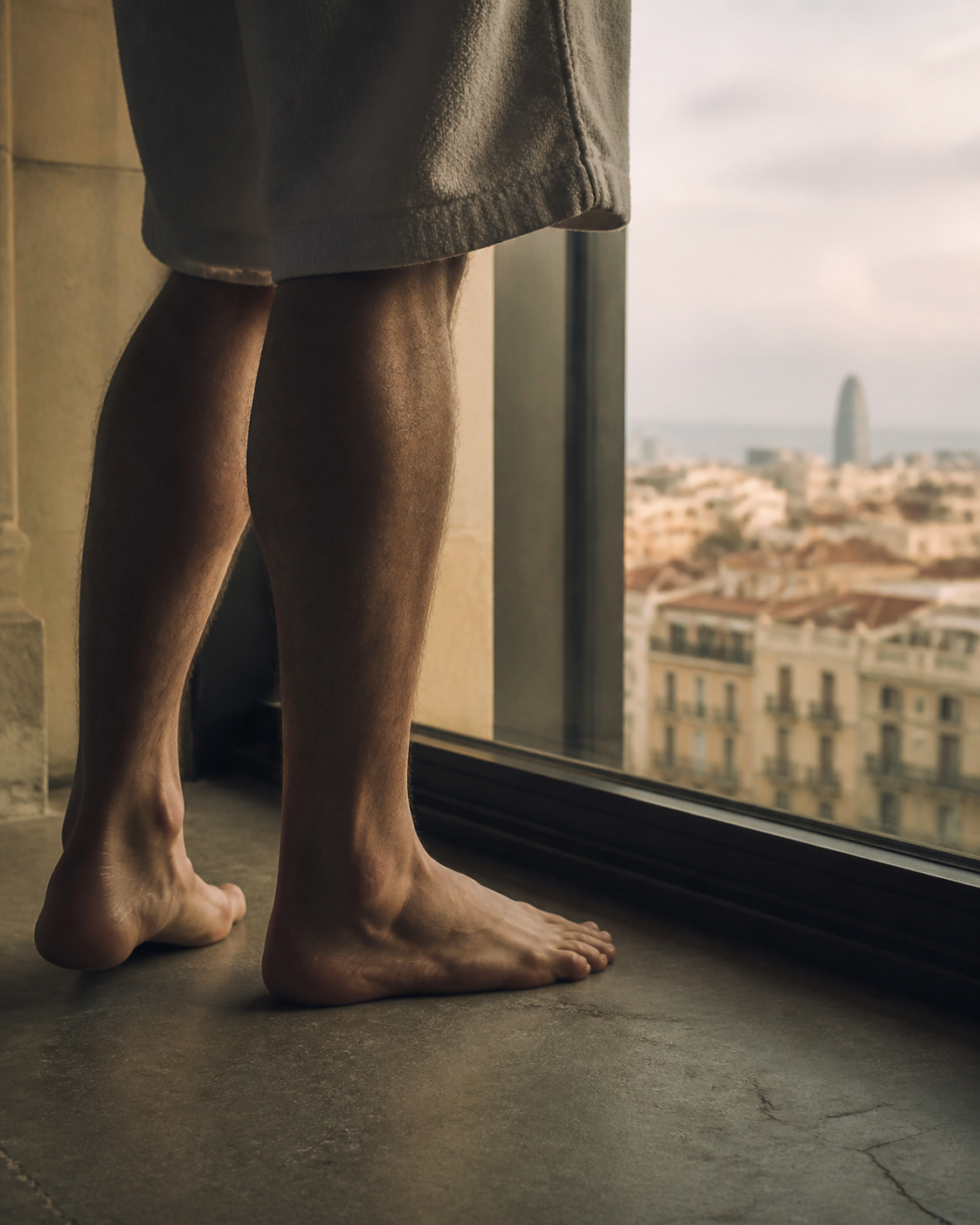Peus masculins descalços sobre terra fred prop d'una finestra amb vista als teulats de l'Eixample de Barcelona: la contemplació de qui aprèn a sostenir el que sent